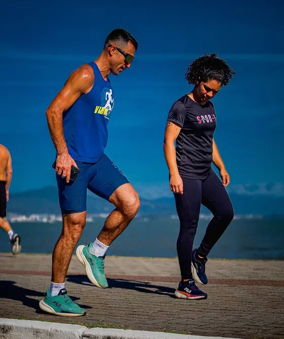 Izaias Vidal demonstrando um exercício educativo de corrida ao lado de uma aluna, com o mar ao fundo